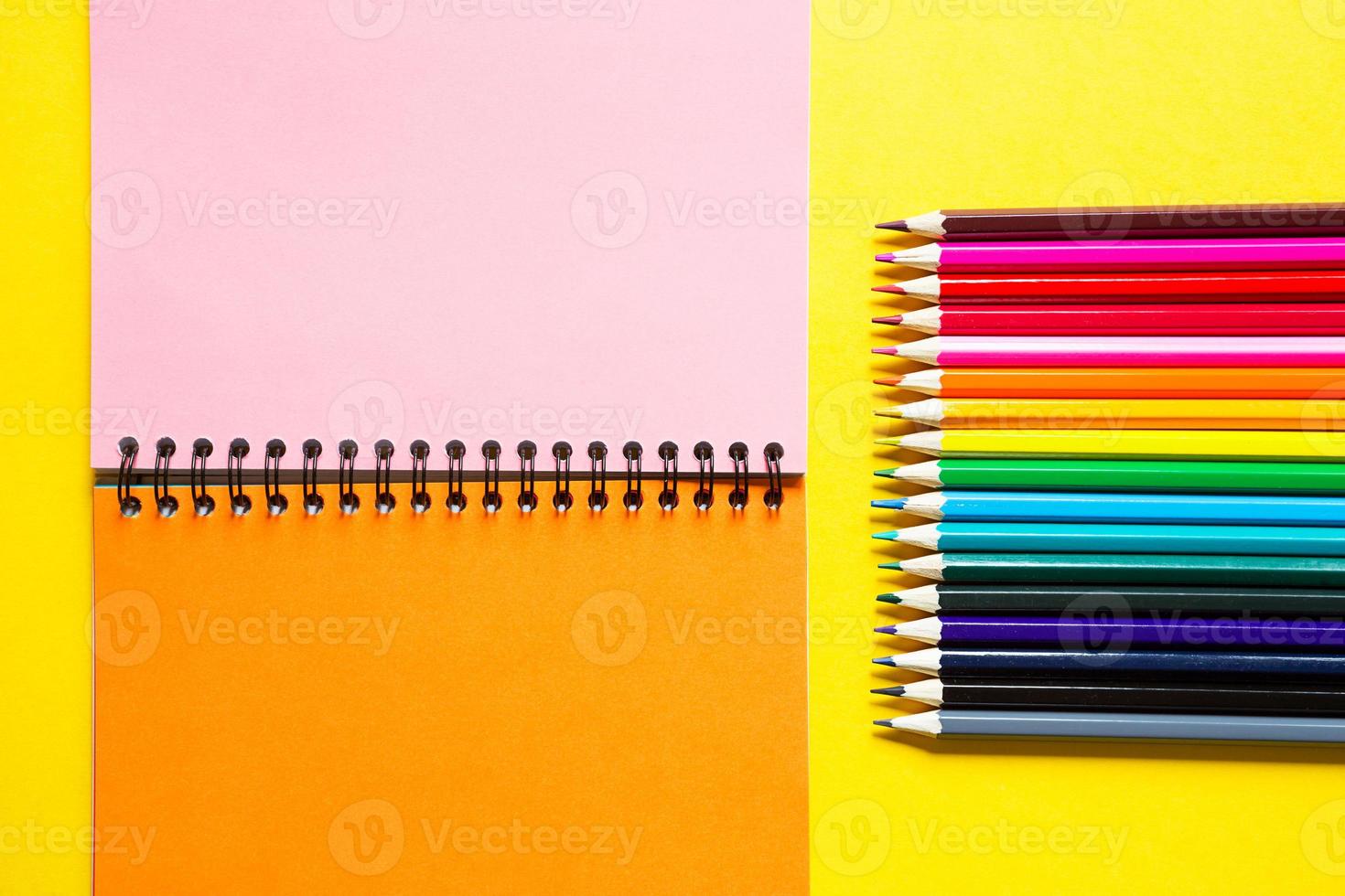 paleta de arco-íris de lápis de cor com um caderno espiral em um fundo amarelo, simulado, postura plana. volta às aulas, recrutamento de alunos, artista, aulas de desenho. copie o espaço. papelaria para criatividade foto