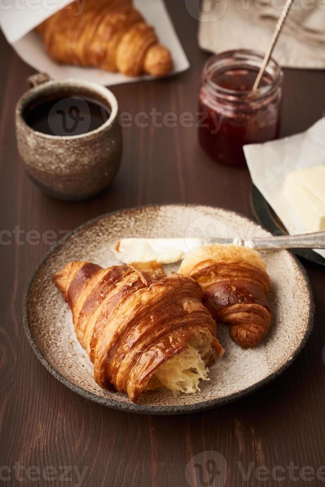 café da manhã com croissant no prato, xícara de café, geléia e manteiga. vertical, vista lateral foto