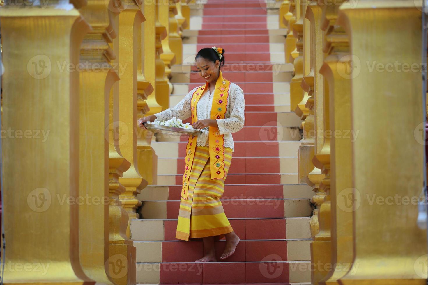 jovem asiática em traje tradicional birmanês, segurando a tigela de arroz na mão no pagode dourado no templo de mianmar. mulheres de mianmar segurando flores com vestido tradicional birmanês visitando um templo budista foto