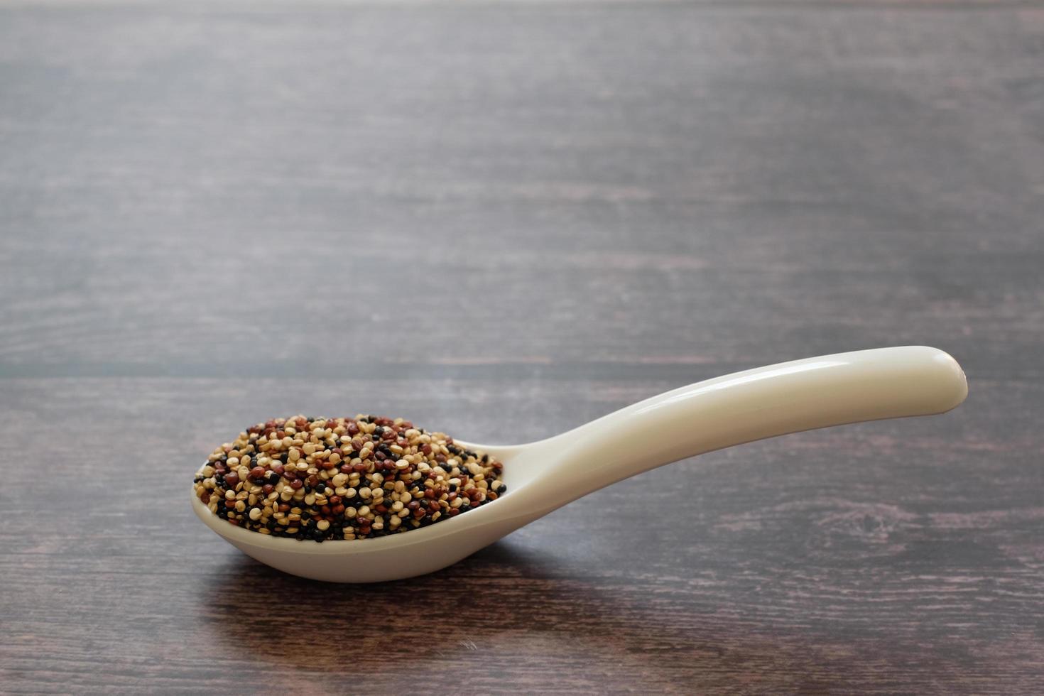 sementes de quinoa na colher branca isoladas no fundo da mesa de madeira. A quinoa é uma boa fonte de proteína para pessoas que seguem uma dieta baseada em vegetais. foto