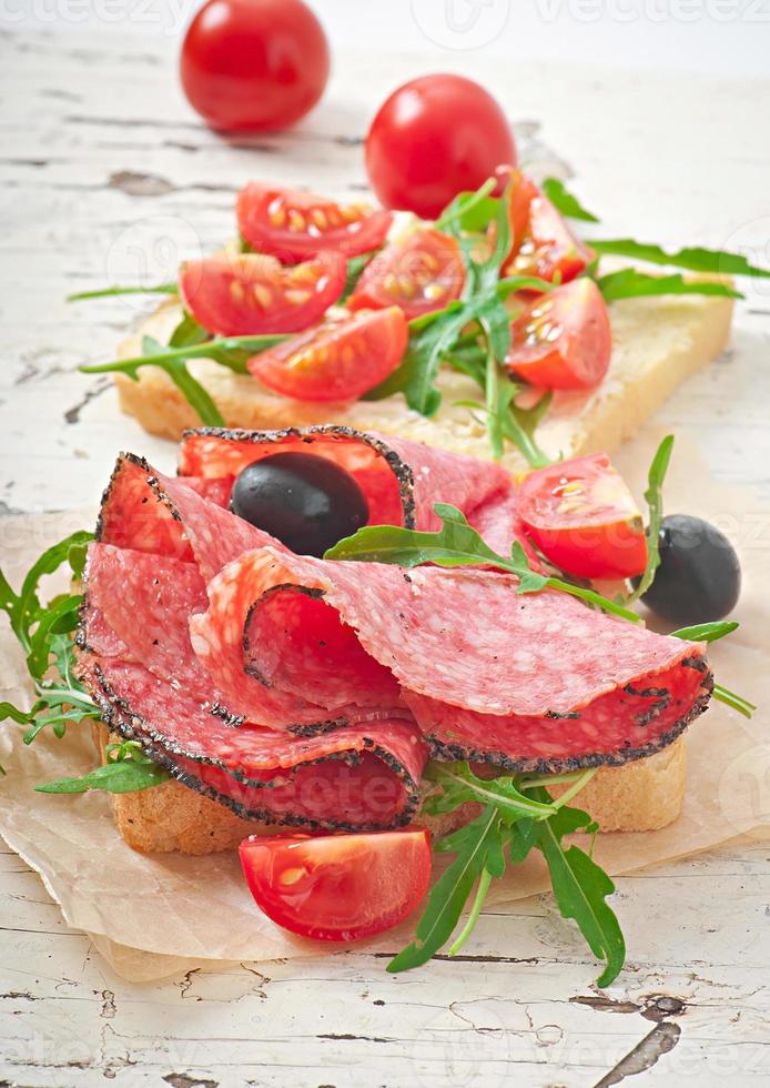 sanduíche com salsicha, azeitona, tomate e rúcula no antigo fundo de madeira foto