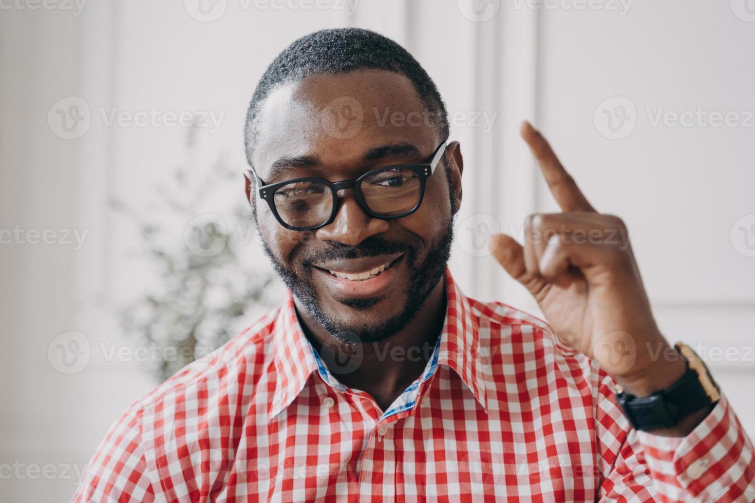 professor de inglês masculino de etnia africana sorridente em óculos levanta a mão aponta com o dedo indicador para cima foto