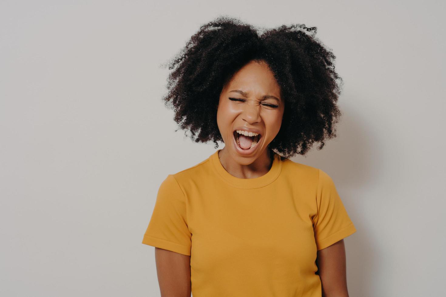 jovem e bela mulher africana com cabelos cacheados, vestindo camiseta amarela casual, gritando com raiva foto