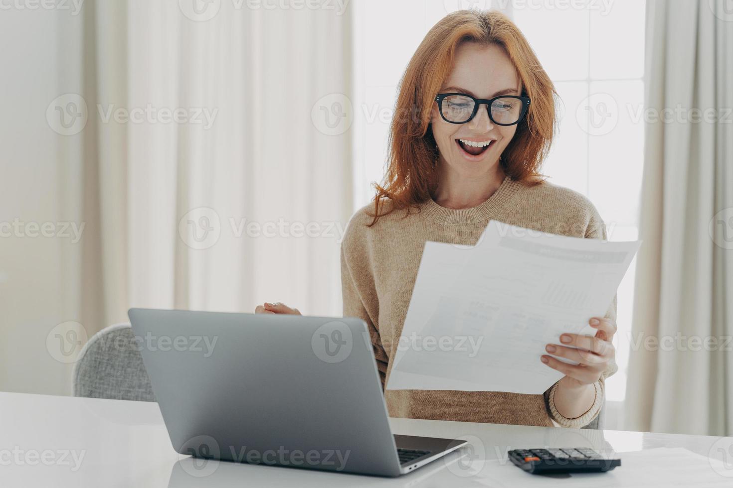 mulher ruiva feliz e animada lendo carta de papel com notificação sobre o último pagamento da hipoteca foto