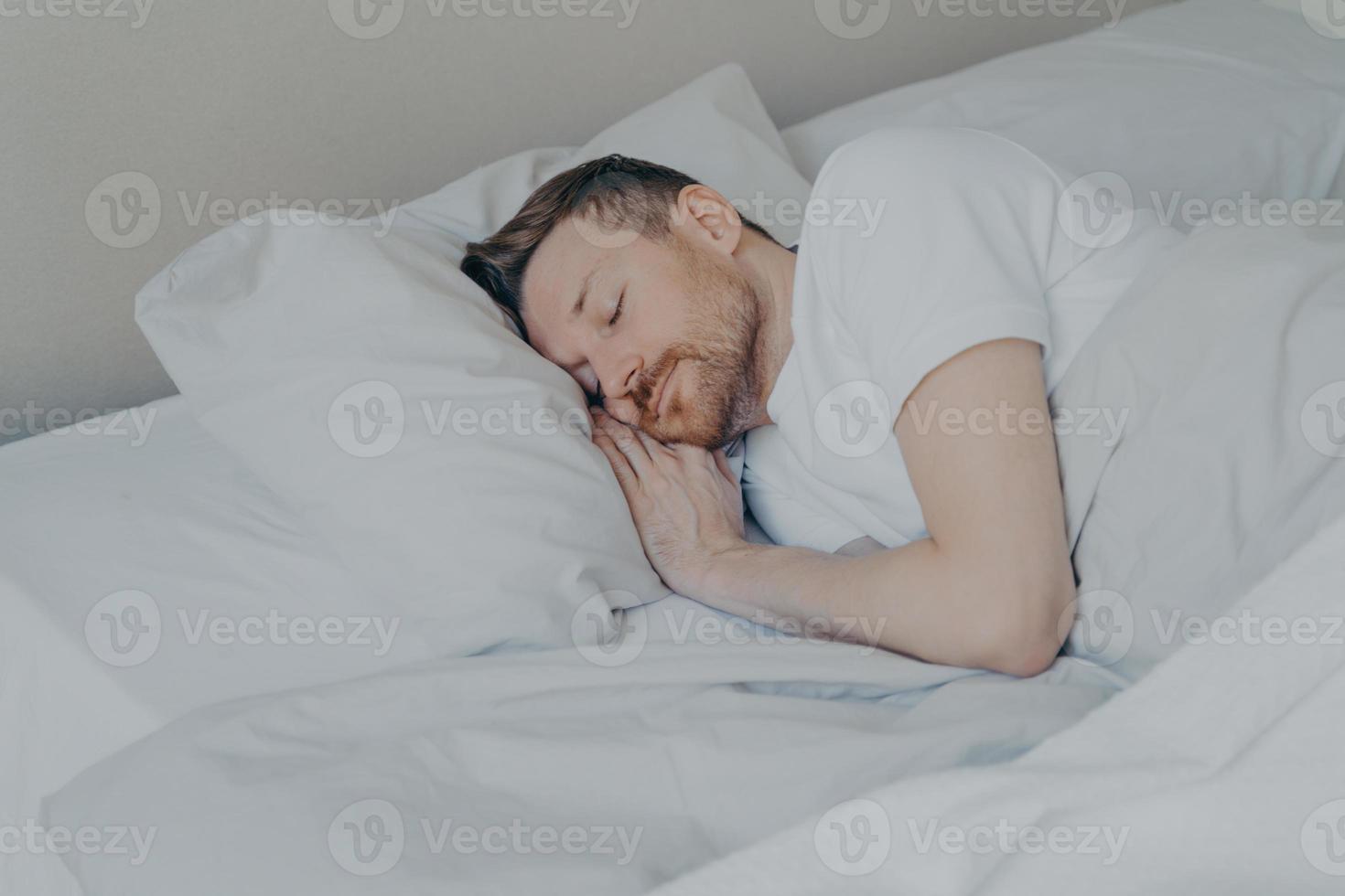 jovem bonito dormindo confortavelmente na cama em casa foto