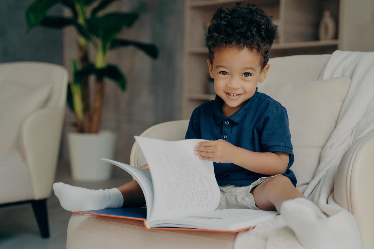 menino afro-americano bonitinho sentado na poltrona com livro de história foto