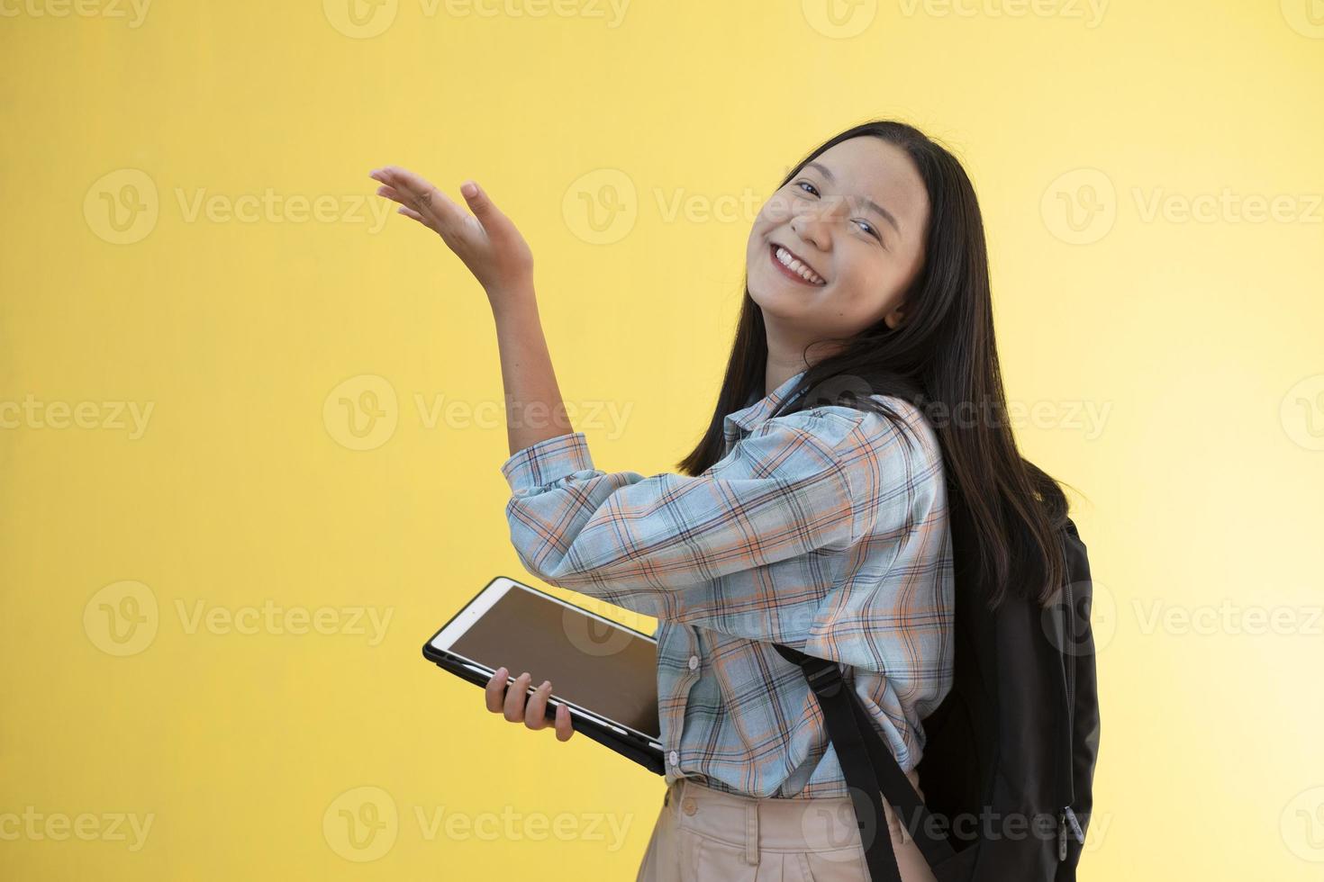 linda jovem com mochila e segure o laptop em fundo amarelo. foto