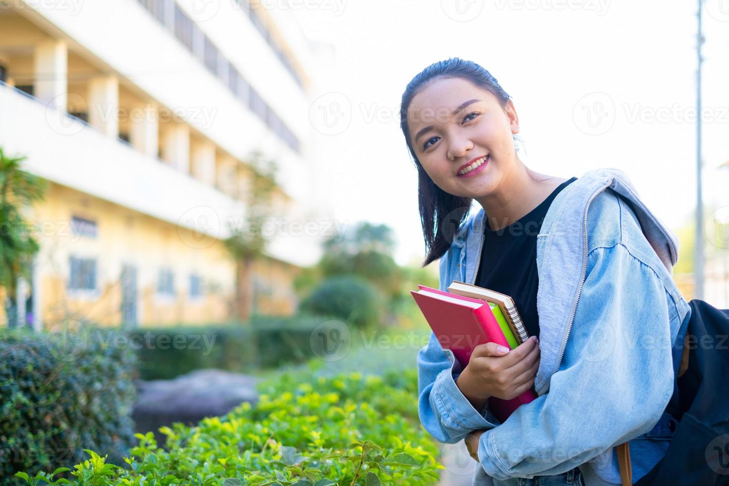 aluna feliz segura livro e mochila na escola, menina asiática. foto