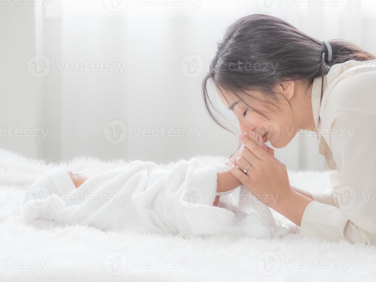 uma linda mulher asiática toca os pés de seu bebê recém-nascido e beija alegremente foto