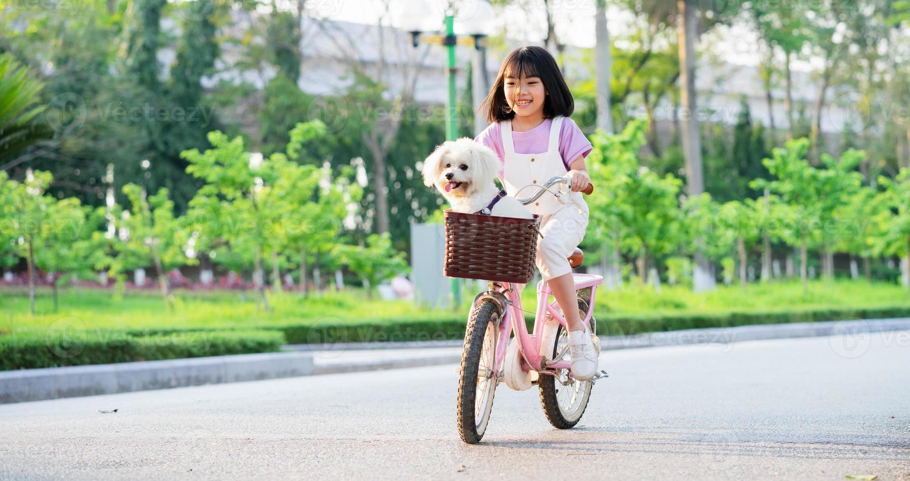 imagem de menina asiática andando de bicicleta com seu cachorro de estimação no parque foto