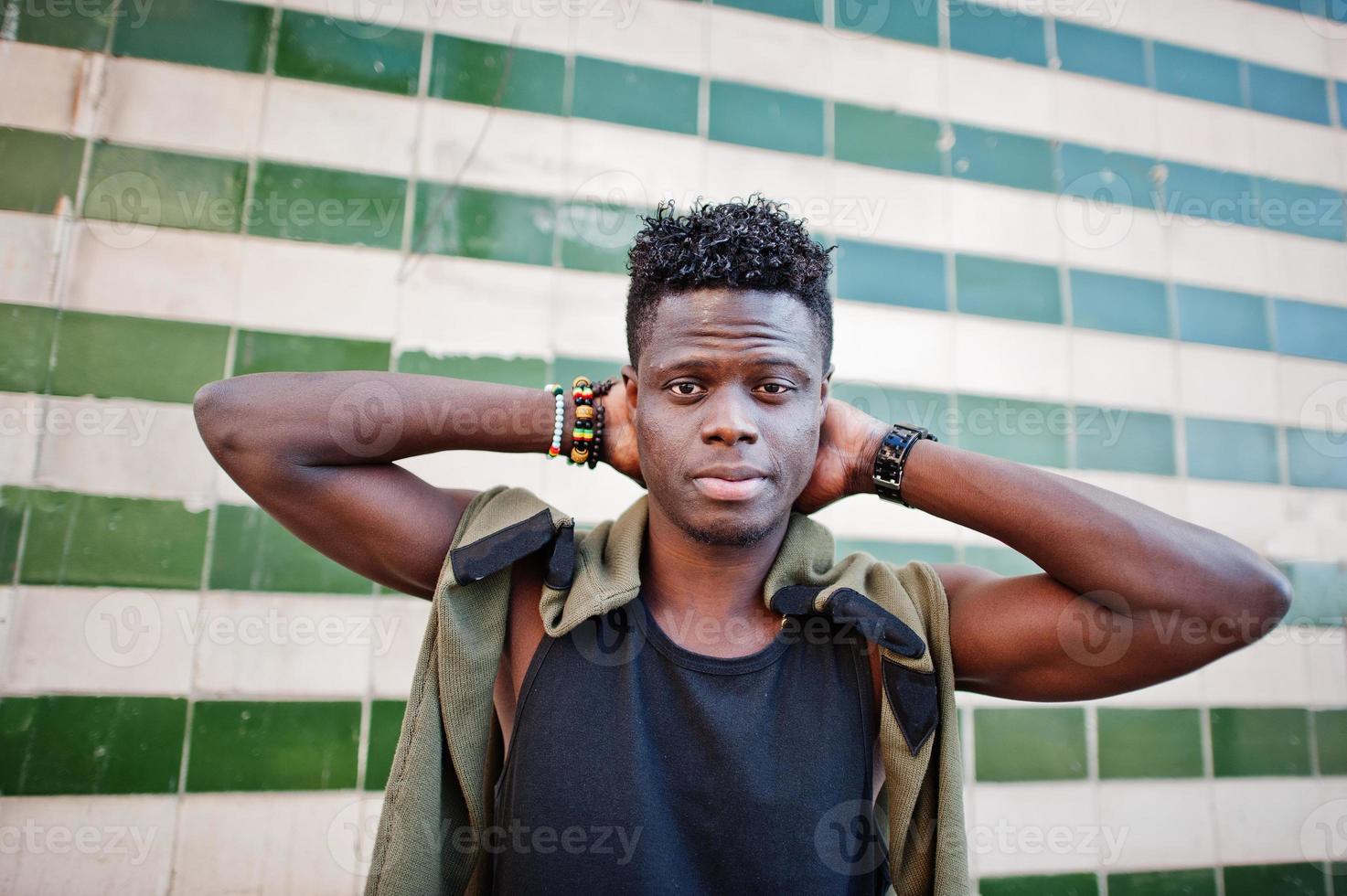 Afro-americano jovem atraente em roupas casuais em pé ao lado da parede de azulejos. foto