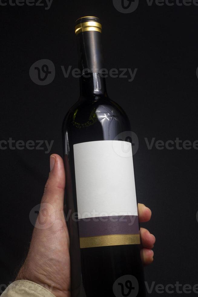 homem segurando a garrafa de vinho tinto isolada no fundo preto. rótulo de maquete foto