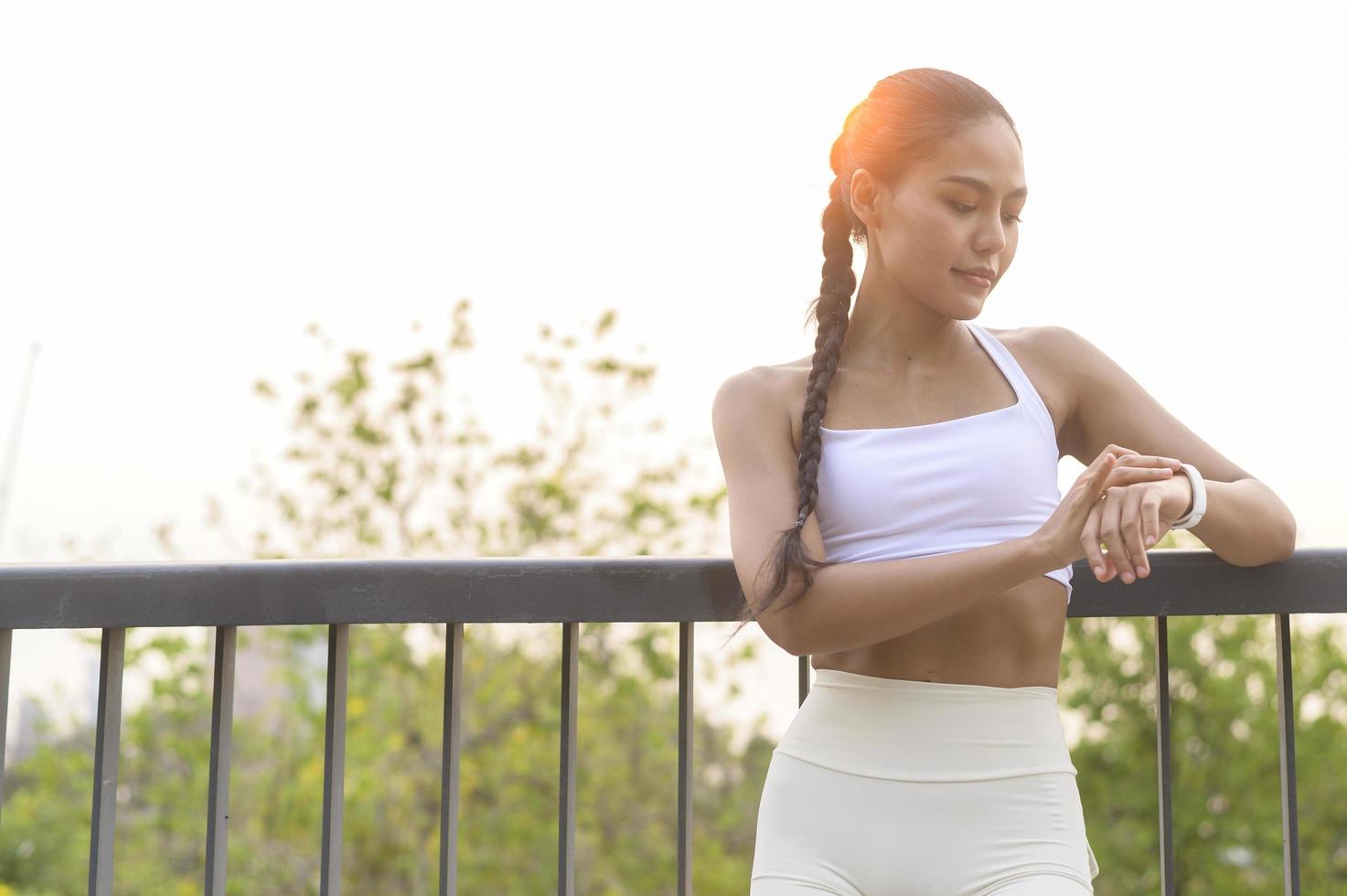 uma jovem fitness em roupas esportivas usando relógio inteligente enquanto se exercita no parque da cidade, saudável e estilos de vida. foto