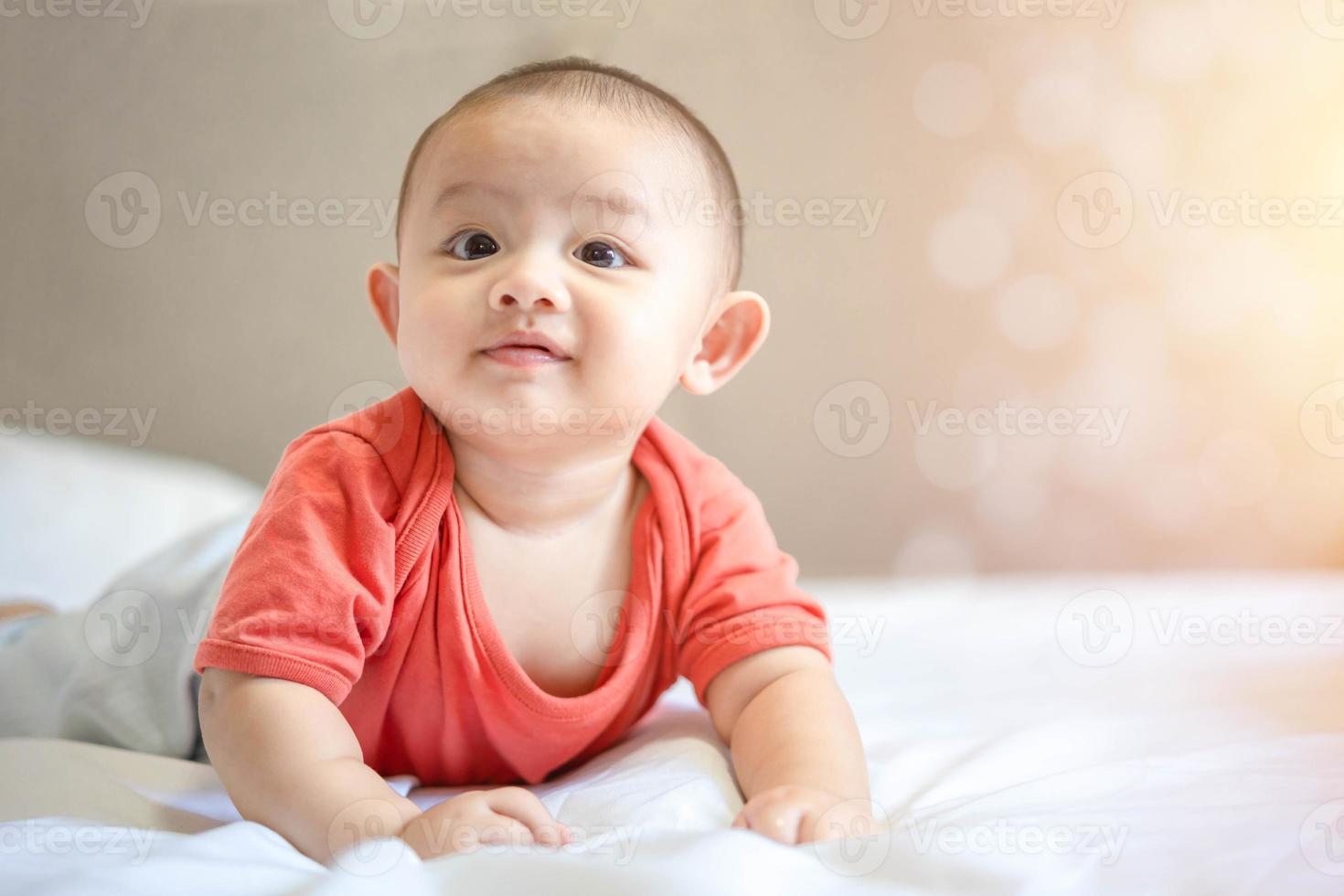 família feliz, bebê recém-nascido asiático fofo usa camisa vermelha deitado, rastejando, brinca na cama branca com sorriso sorridente rosto feliz. criança adorável infantil inocente no primeiro dia de vida. conceito de dia das mães. foto