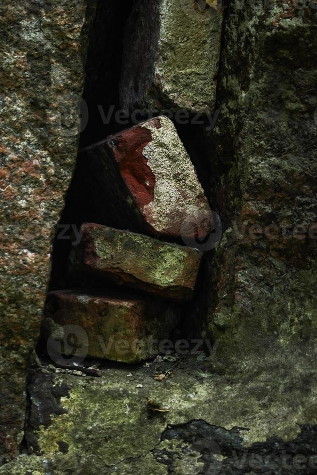 tijolos sujos velhos empilhados em um buraco entre paredes cobertas de musgo foto