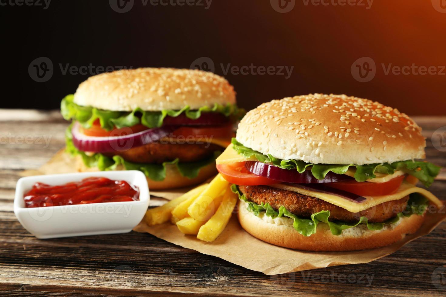 imagem de 2 hambúrgueres em uma mesa de madeira com batatas fritas e ketchup foto