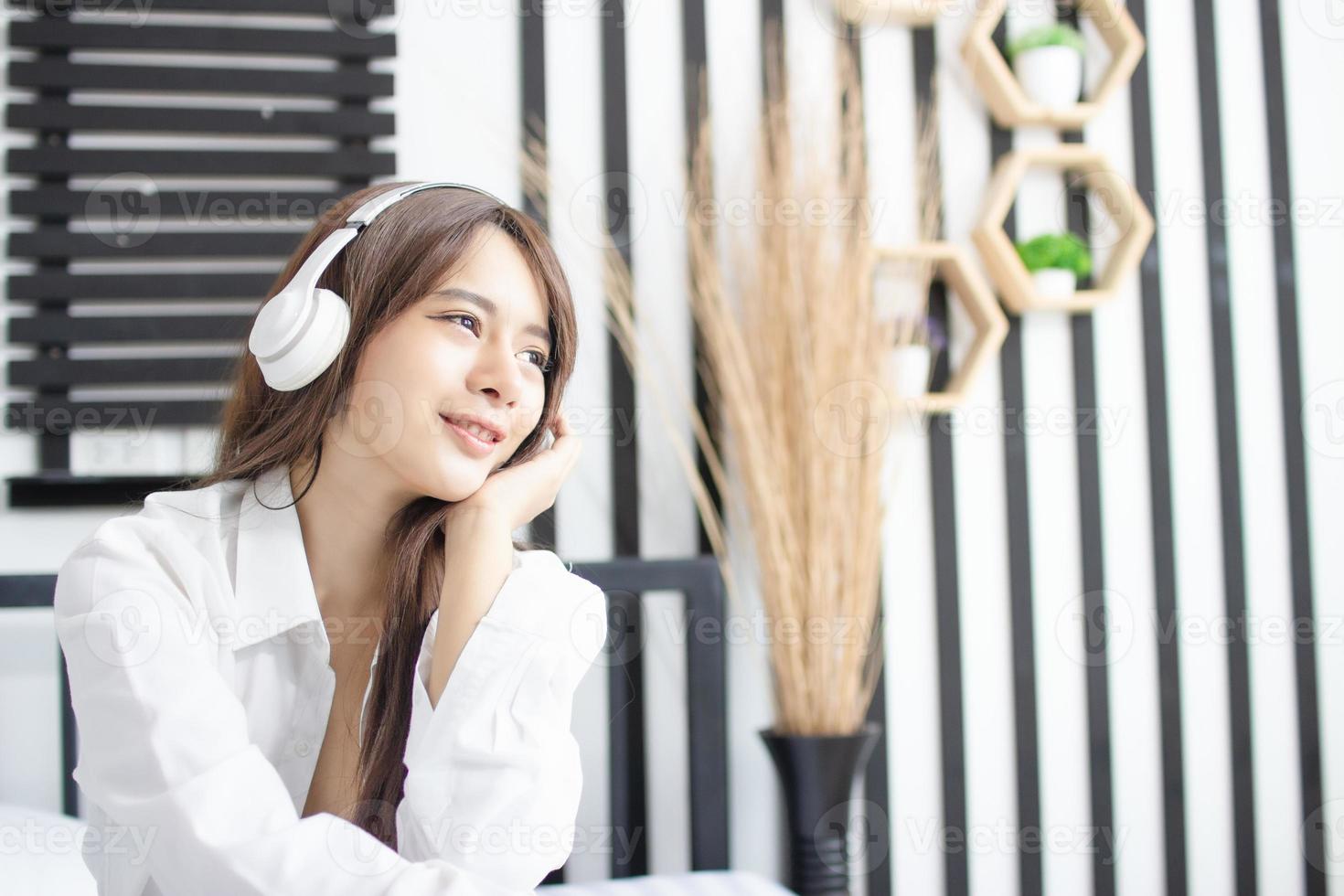 retrato jovem sorriso feliz linda mulher asiática relaxar quarto. mulher com fones de ouvido tocando violão no quarto branco foto