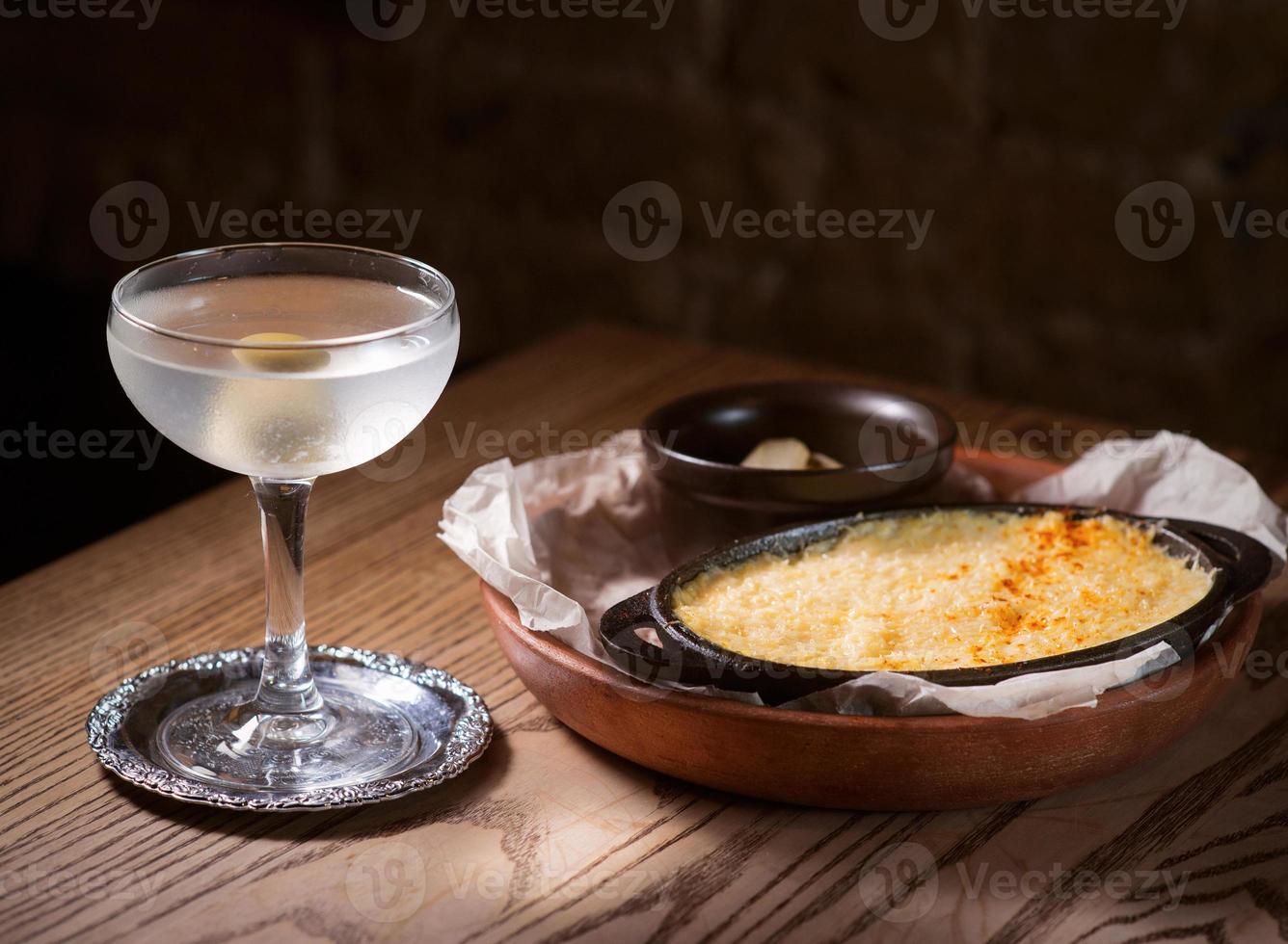 peixe assado com queijo e pepinos salgados e coquetel de álcool com azeitona na mesa foto