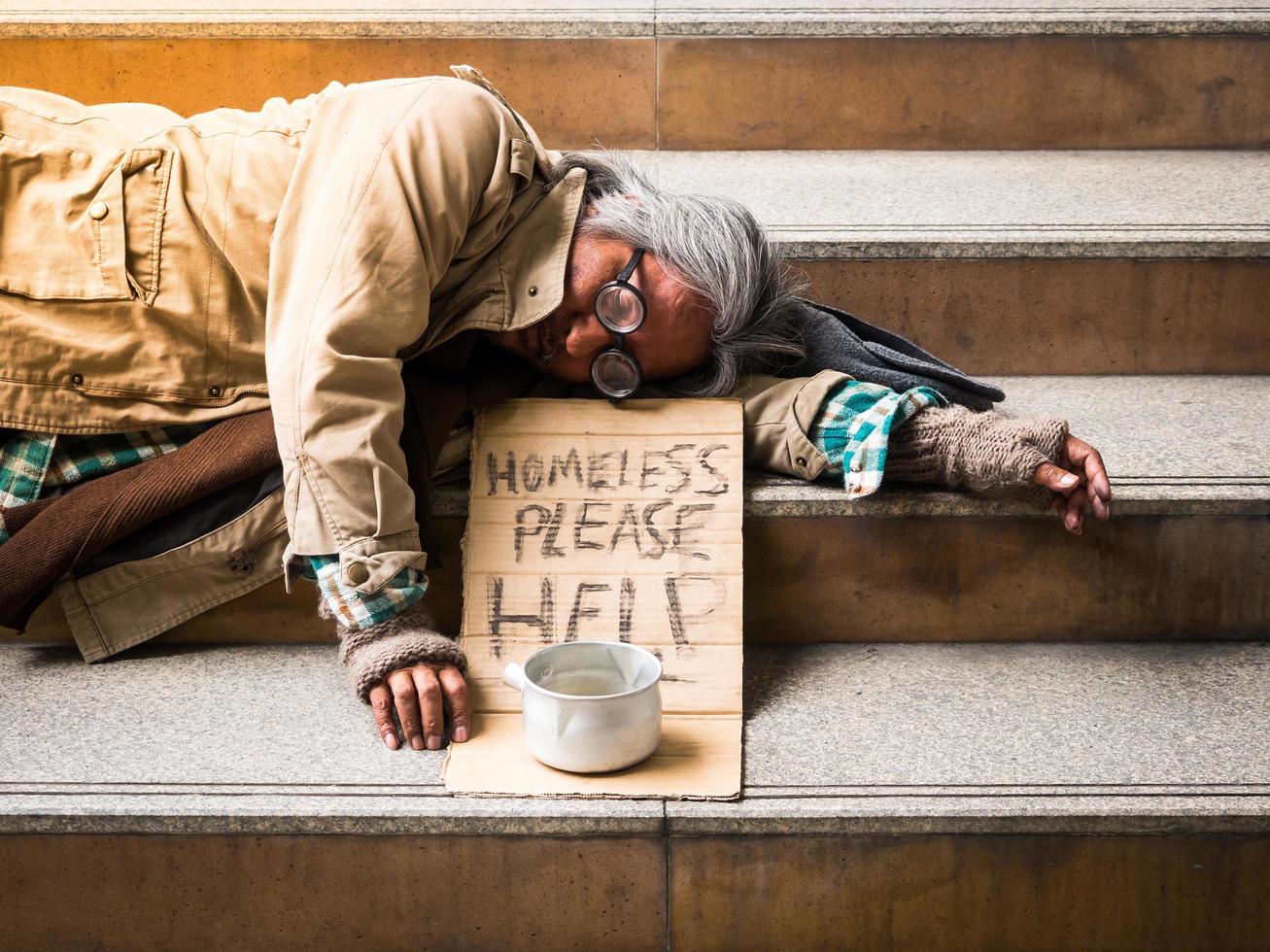 um pobre sem-teto dorme em uma escada com uma conta de doação foto