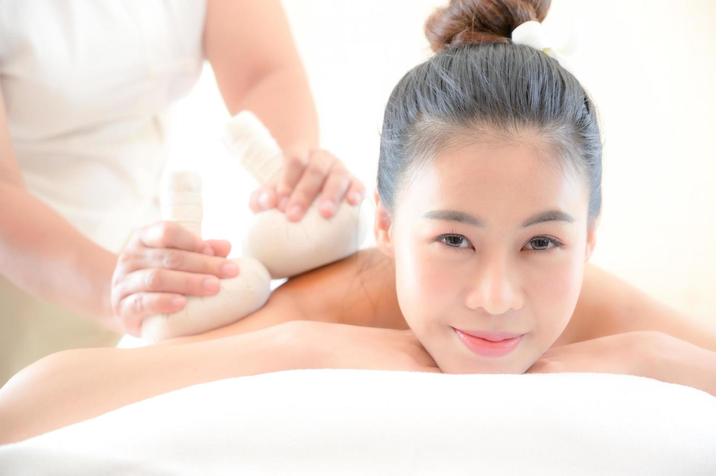 uma linda mulher asiática é descontraída e relaxante, a massagista usa uma compressa de ervas quente em uma loja de spa foto