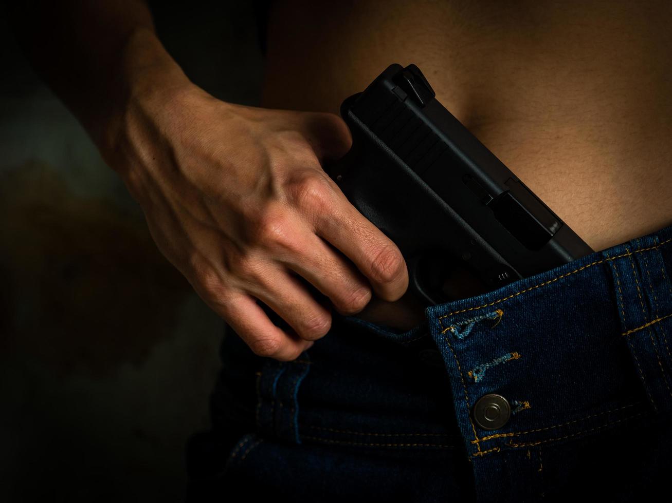 mãos de jovem com arma em seu jeans azul foto