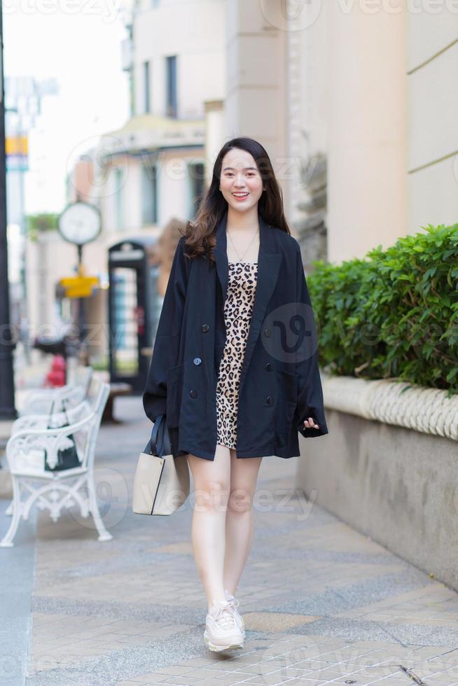 mulher bonita asiática está sorrindo alegremente que segura a bolsa na mão e andando na cidade. foto
