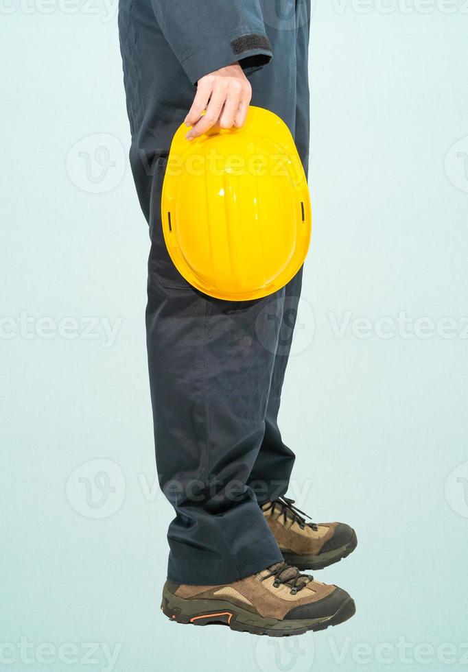 trabalhador de macacão azul segurando capacete amarelo foto