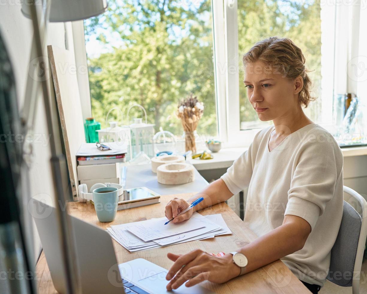 designer de jovem empreendedora escrevendo na folha de papel, mulher séria pensando e planejando foto