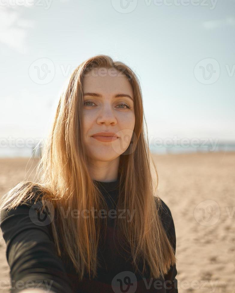 mulher bonita com cabelo comprido, loira tomando selfie no celular na praia no verão foto