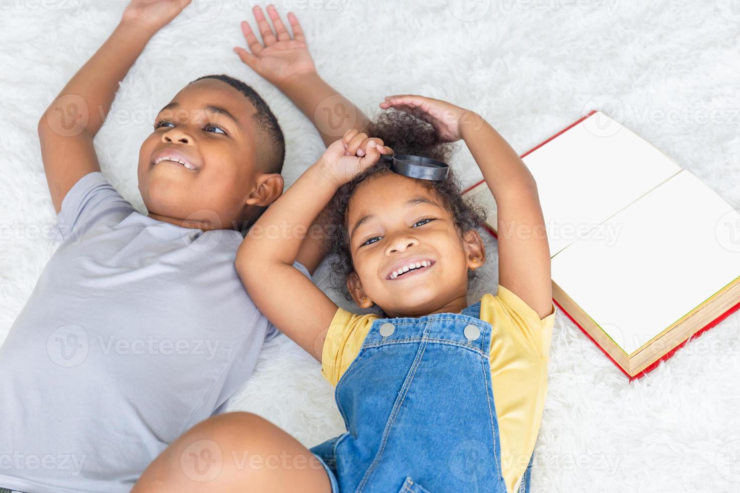 retrato de alto ângulo de duas crianças deitadas no chão branco e olhando para a câmera, feliz irmã e irmão brincando na sala de estar foto