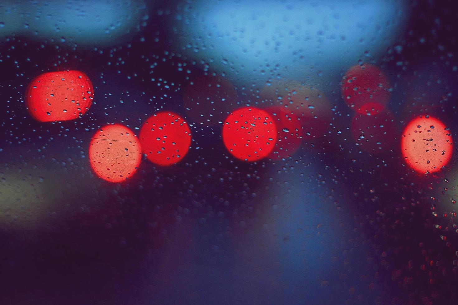 gotas de chuva no vidro do carro e luz colorida de bokeh de trânsito foto