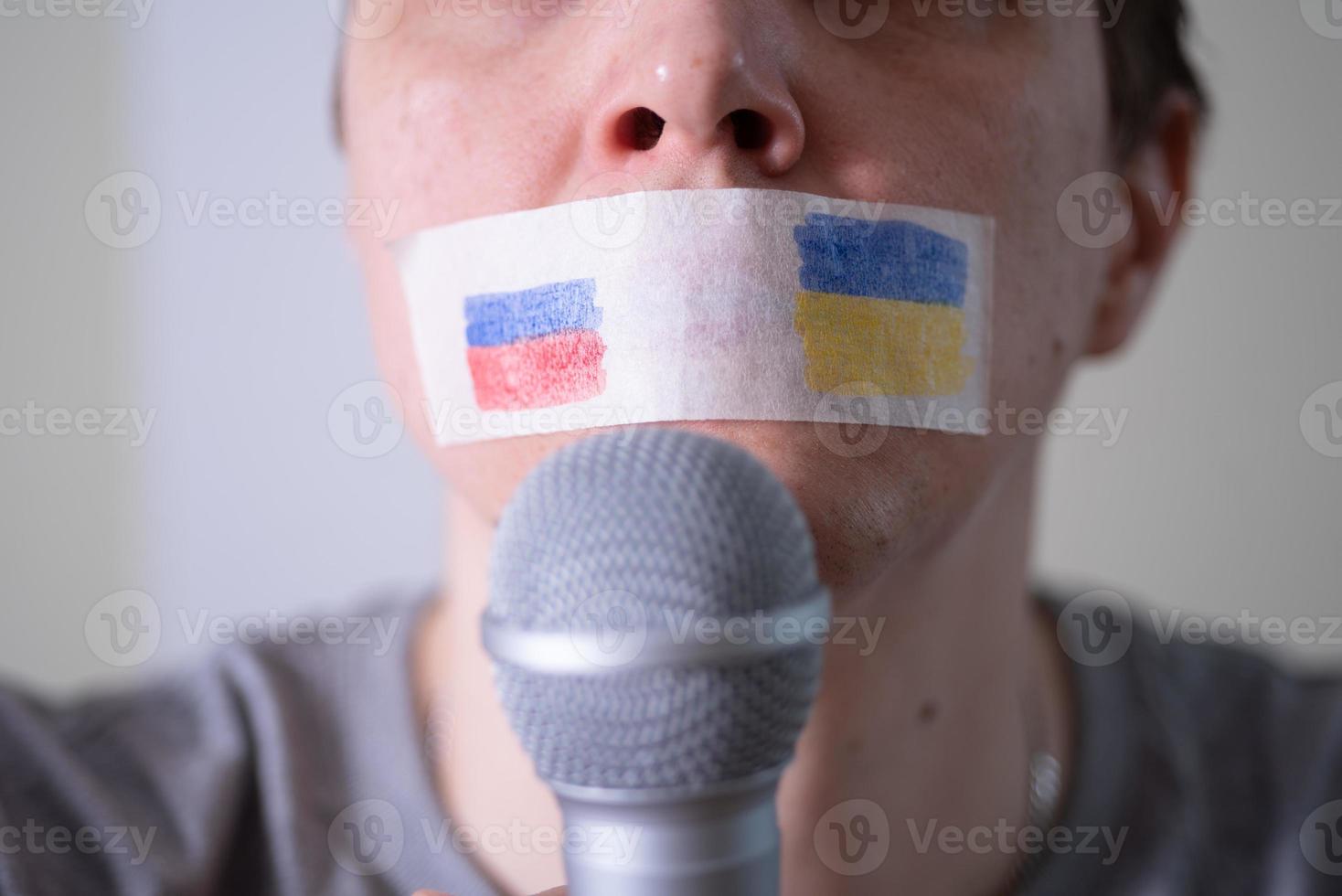 uma boca com fita adesiva com uma bandeira da rússia e da ucrânia tentando falar em um microfone. foto