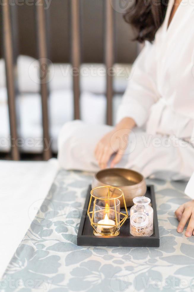 erva de aromaterapia e vela no quarto escuro na cama com mulher asiática sente-se ao lado dele. foto