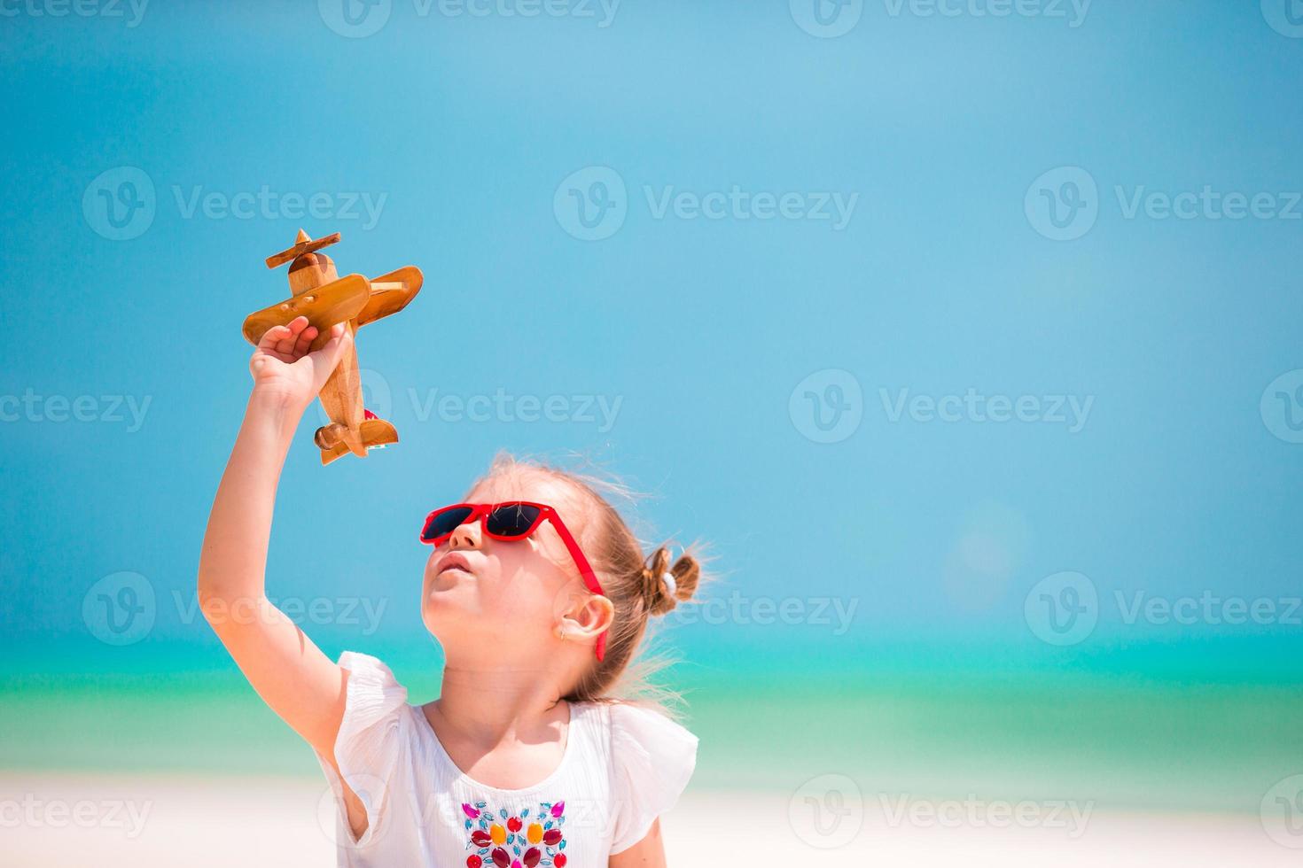 menina feliz com avião de brinquedo nas mãos na praia de areia branca foto