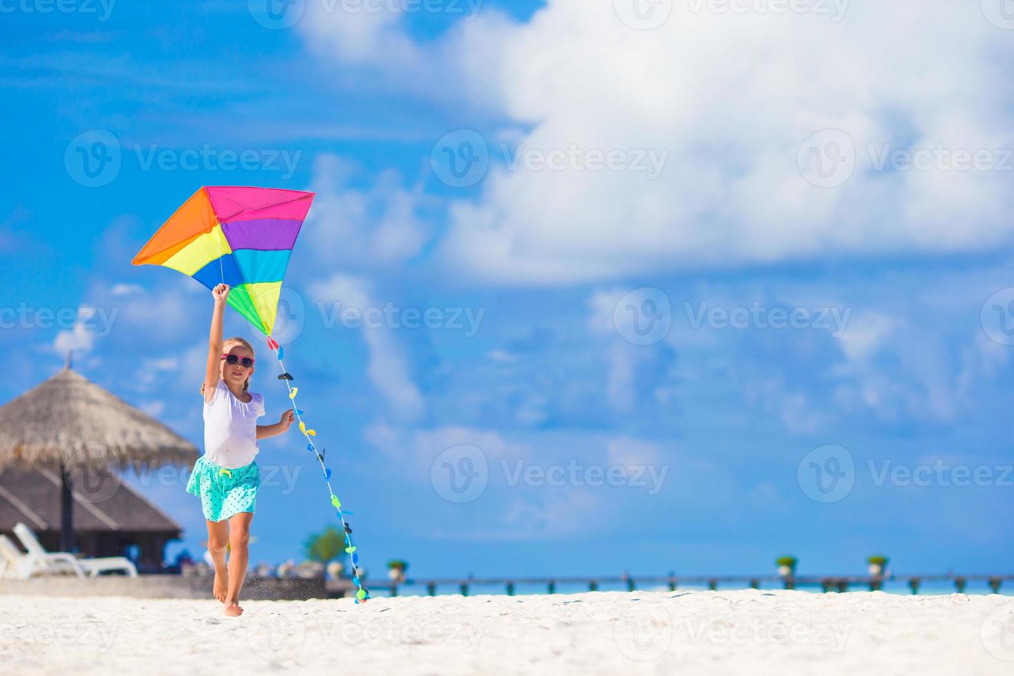 menina feliz brincando com pipa na praia tropical foto