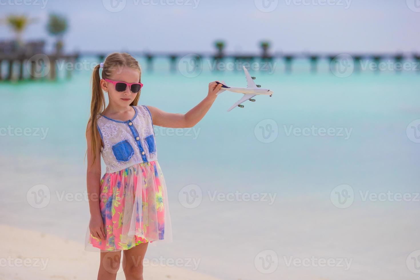 menina feliz com avião de brinquedo nas mãos na praia de areia branca foto