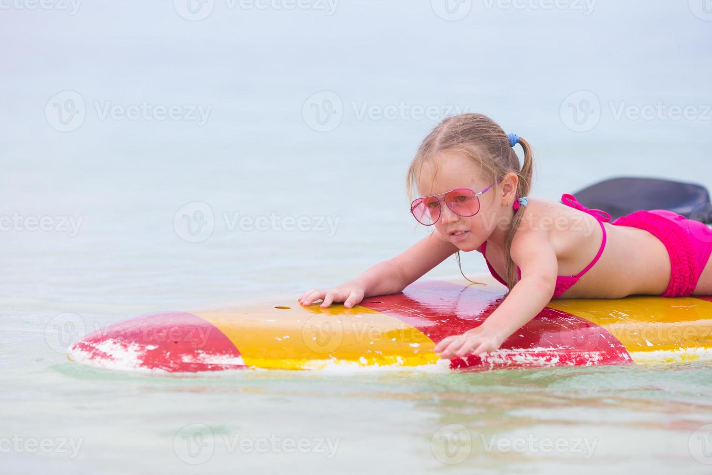 menina adorável em uma prancha de surf no mar turquesa foto