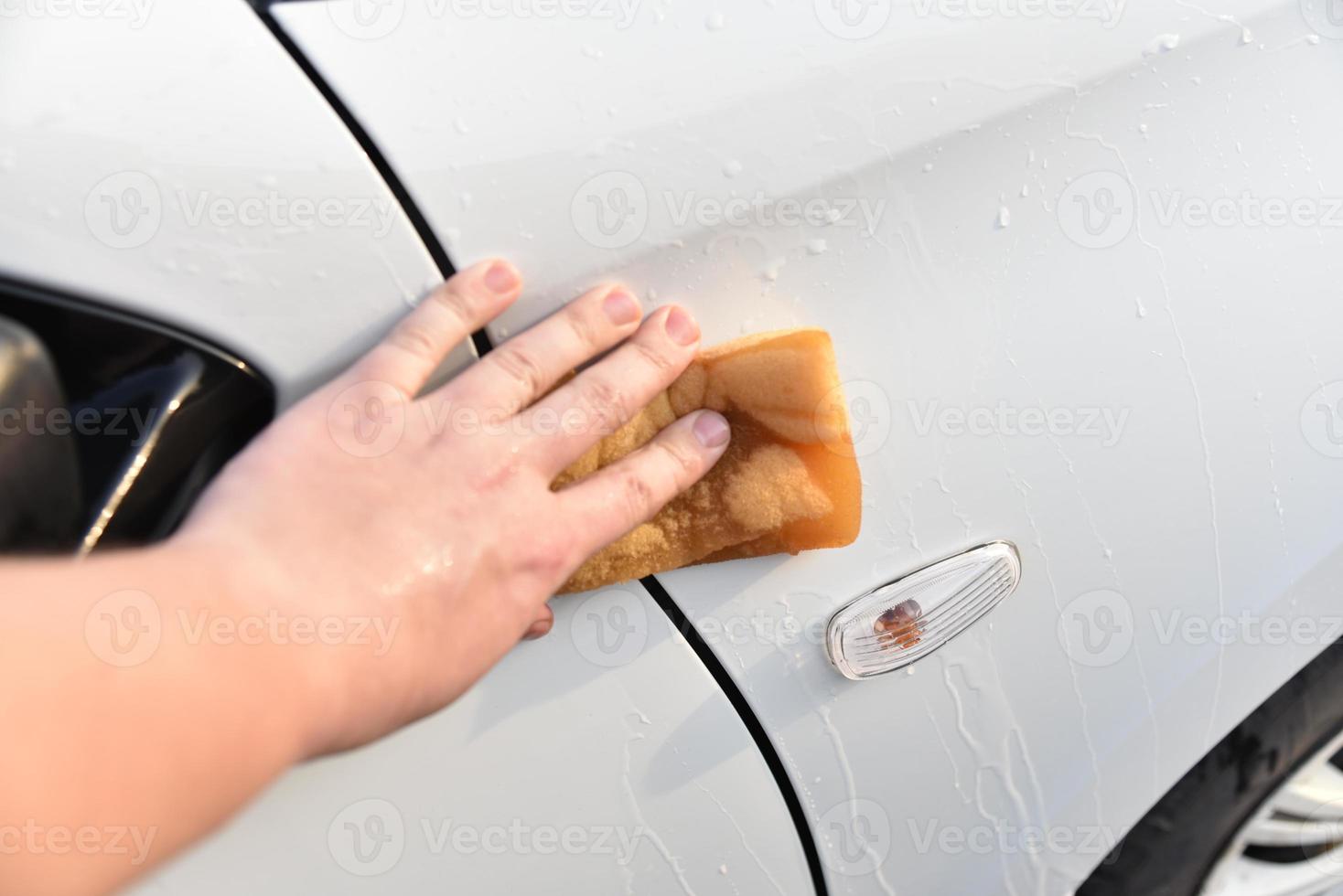lavando um carro branco com uma esponja à mão foto
