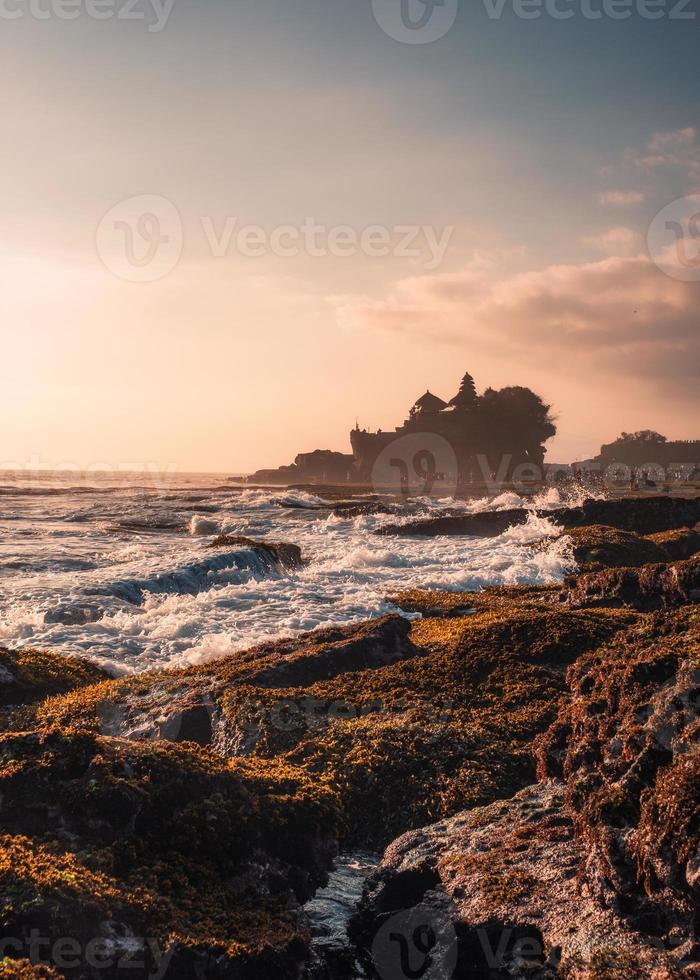 templo puro tanah muito no topo da falésia e onda batendo na praia do pôr do sol em bali foto