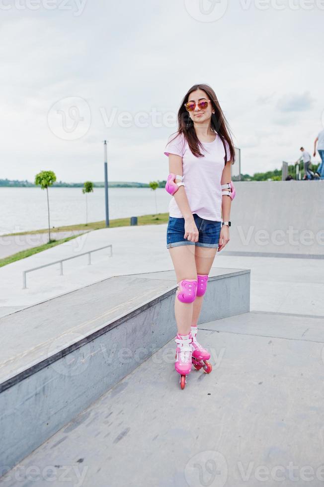 retrato de uma linda jovem em shorts, camiseta e óculos de sol em pé ao ar livre em patins. foto