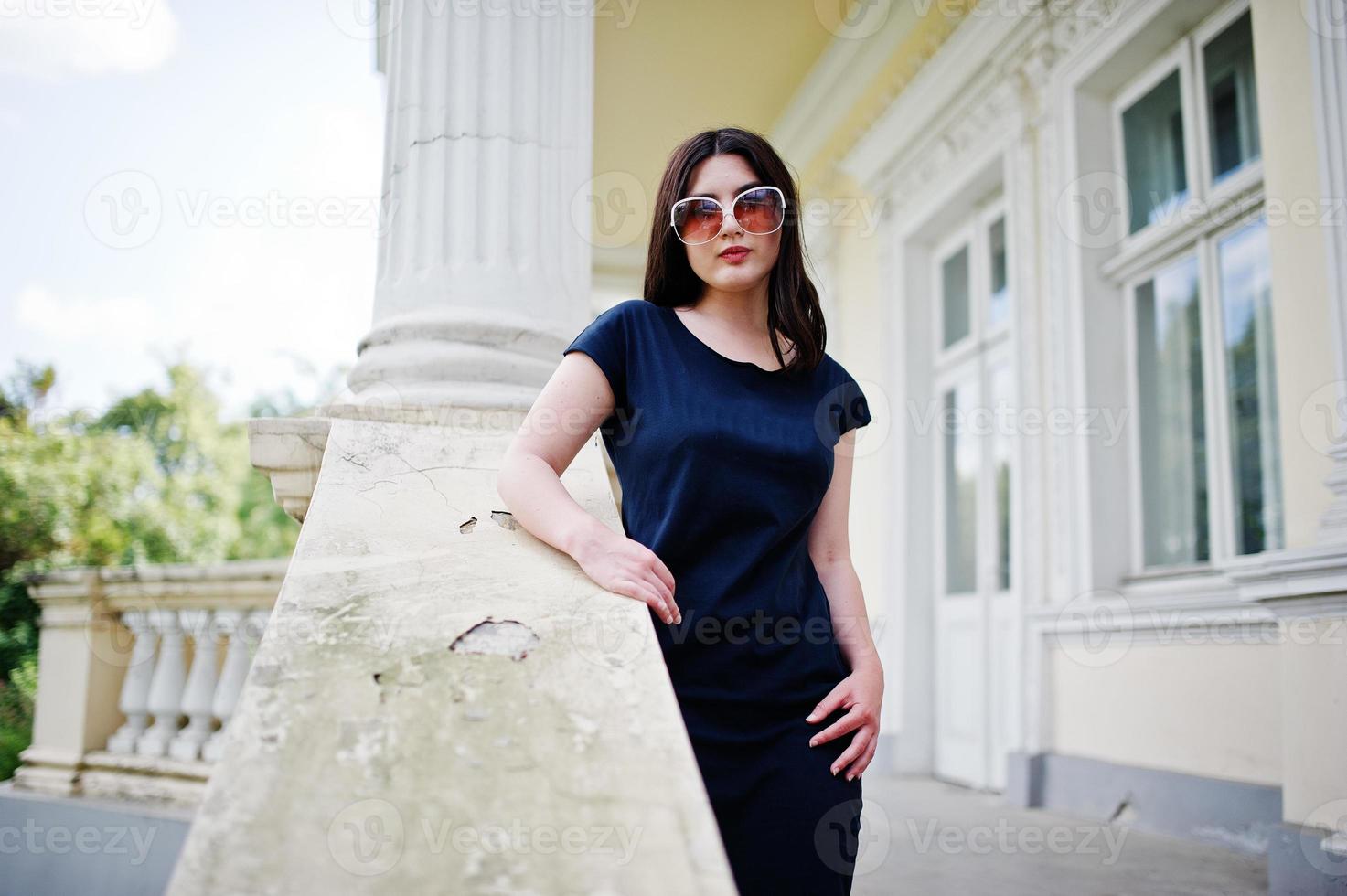 menina morena de vestido preto, óculos de sol posou contra a velha casa vintage, na rua da cidade. foto