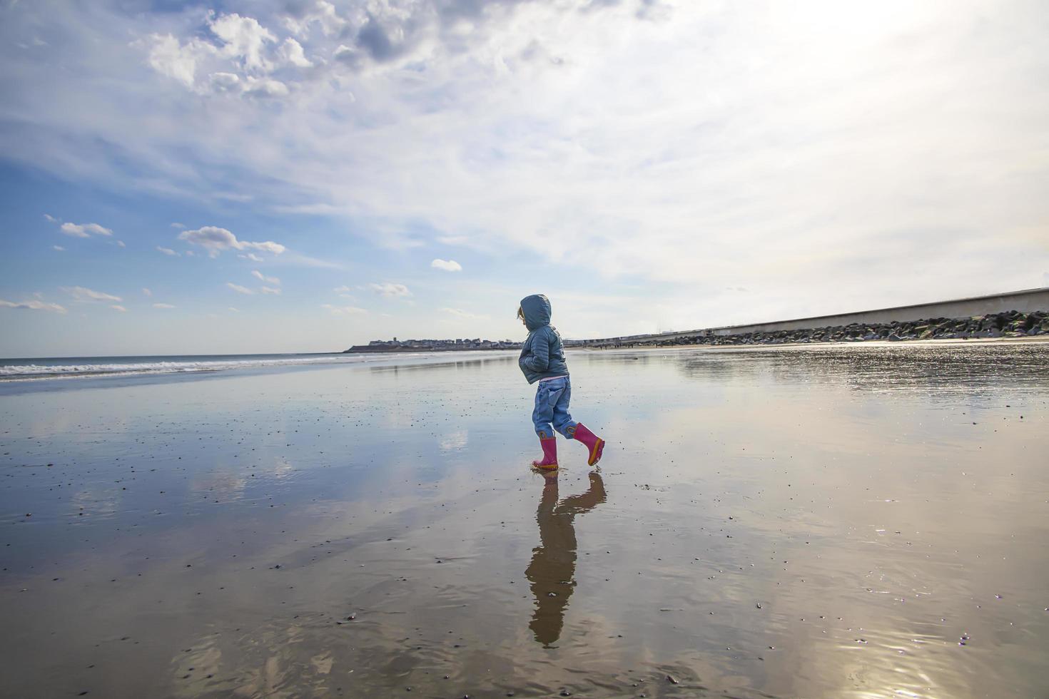 menina com botas cor de rosa andando na praia foto