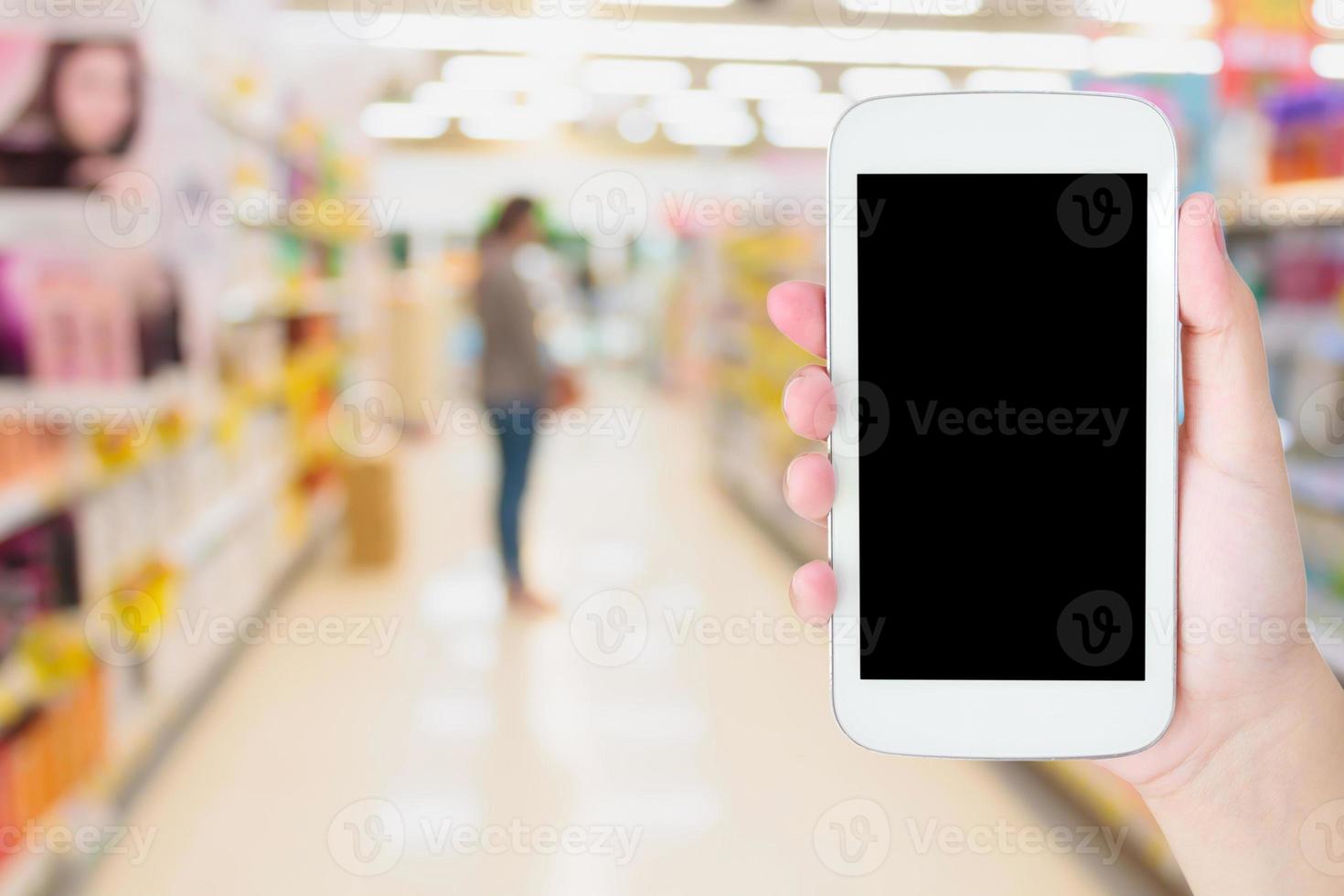 mão feminina segurando o celular no supermercado fundo desfocado foto