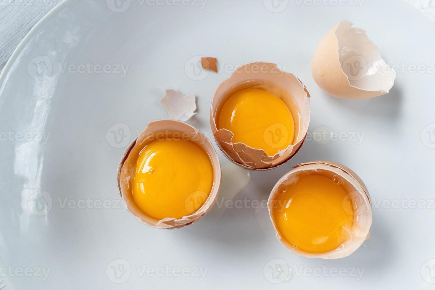 grupo de gemas de ovos em cascas quebradas na postura plana de fundo branco foto