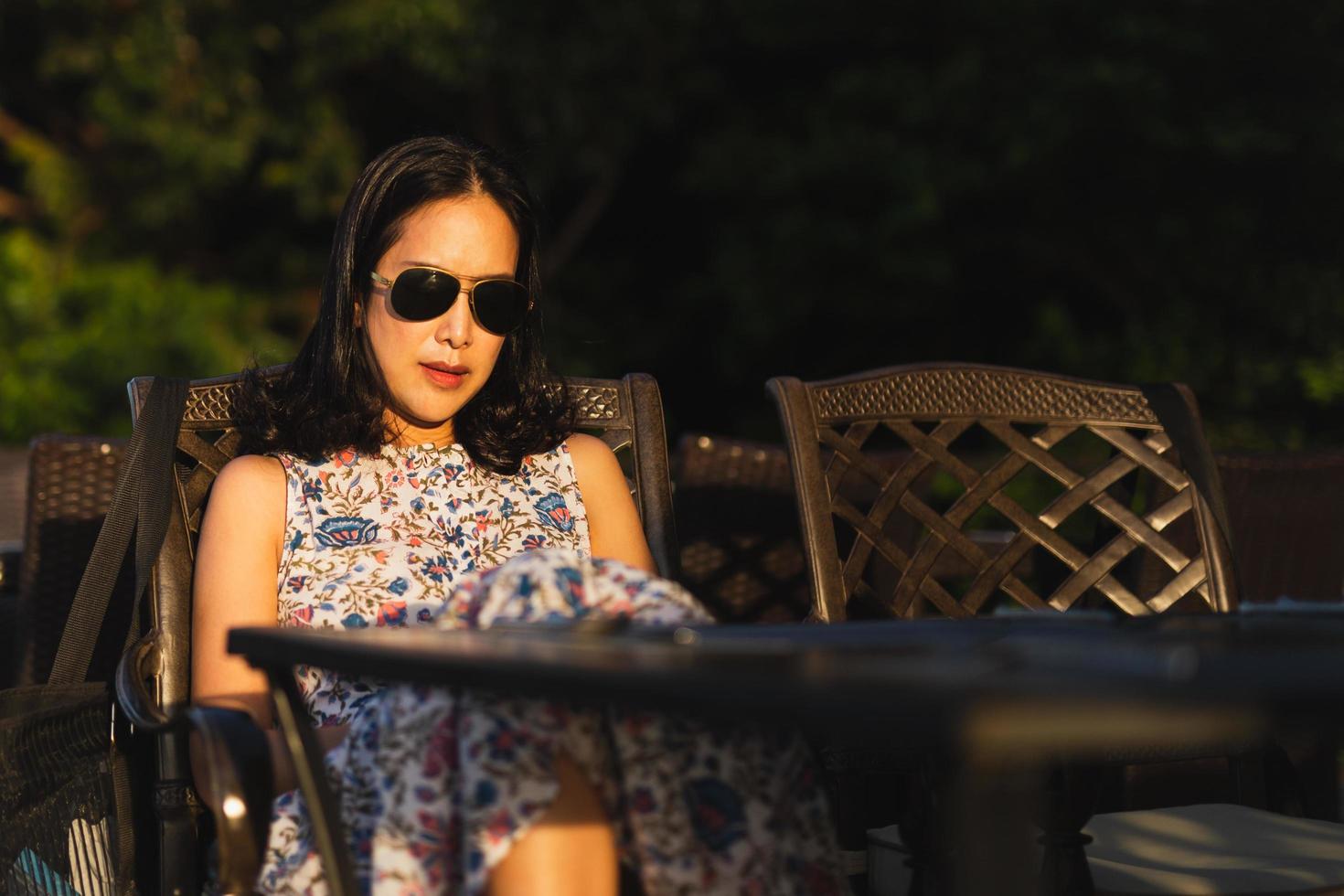 retrato de mulher asiática usando óculos escuros relaxantes no restaurante ao ar livre ao pôr do sol. foto