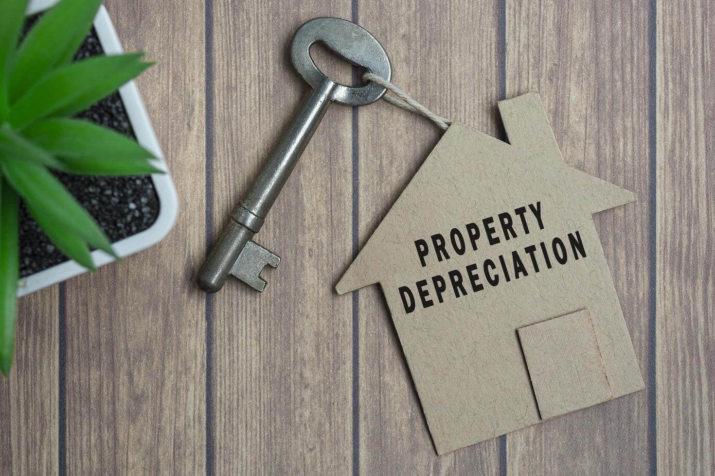 texto de depreciação de propriedade no modelo de casa e chave na mesa de madeira foto