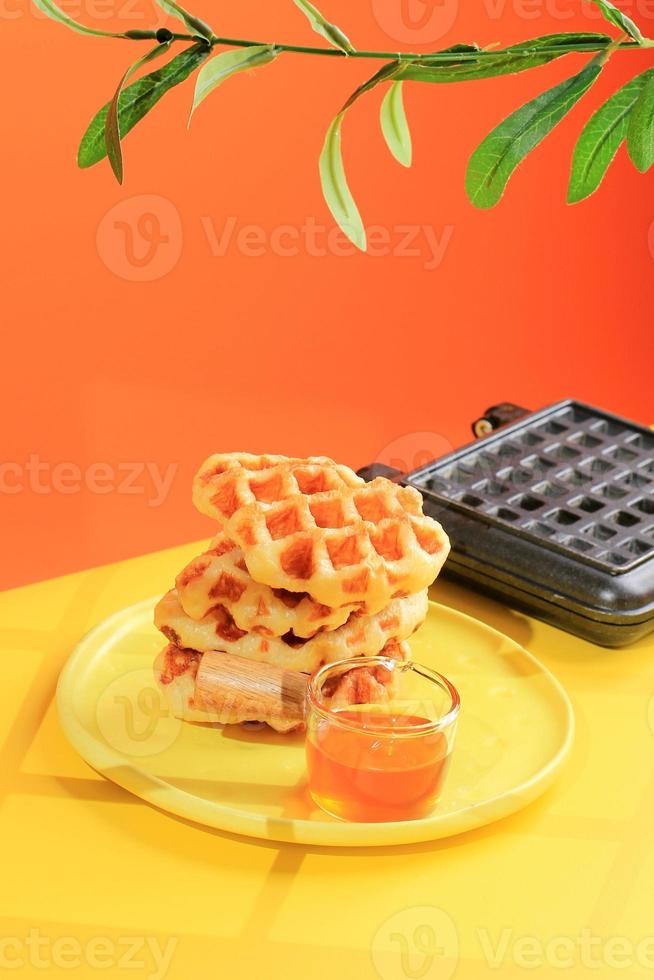 waffle de croissant empilhado na mesa amarela e fundo laranja. croffle é um bolo viral da coreia do sul. comida de cor pop de conceito, copie o espaço para texto foto