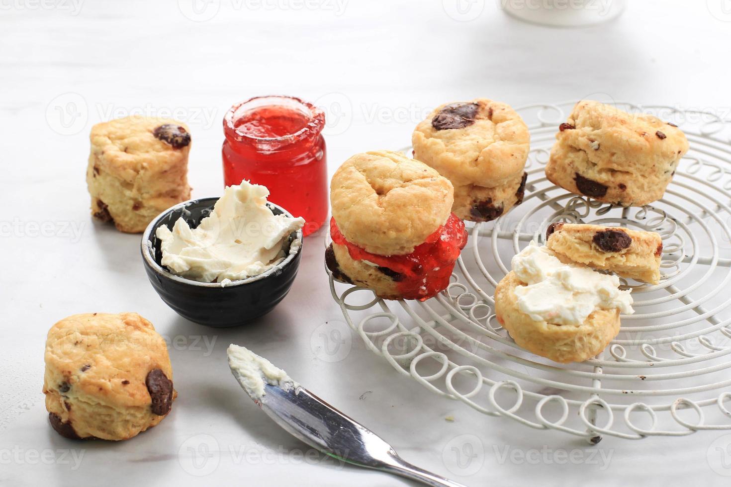 mini scones redondos com geléia de morango e creme de leite e uma xícara de chá, fundo de mármore branco foto