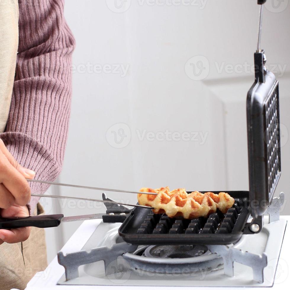 mão do chef pega croffle do fogão, preparação fazendo waffle de croissant ou croffle de massa de croissant congelada foto