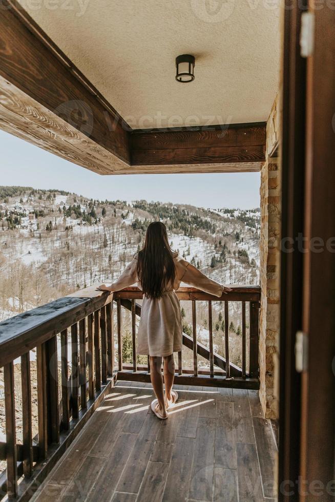 encantadora jovem de roupão de banho apreciando a natureza do inverno no grande terraço foto